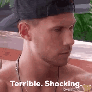 a shirtless man wearing a baseball cap and a necklace is eating a piece of food and says terrible shocking .