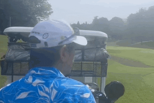 a man wearing a white hat and a blue shirt is driving a golf cart on a golf course .