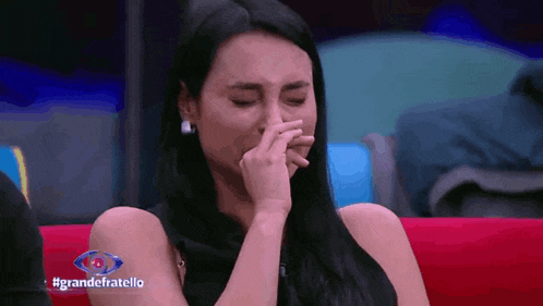 a woman is crying while sitting on a red couch with #grandefratello written on the screen