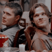 two men are sitting back to back at a table with candles .