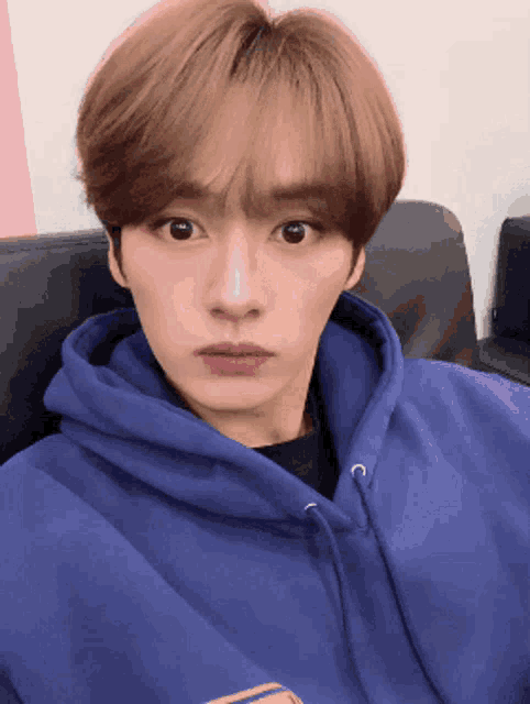 a young man wearing a blue hoodie is sitting on a couch