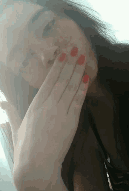 a woman with red nails covering her face with her hand