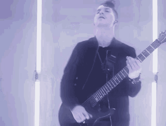 a man in a black jacket is playing a guitar in front of a purple background .