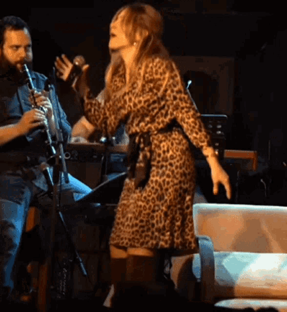 a woman in a leopard print dress sings into a microphone while a man plays a clarinet