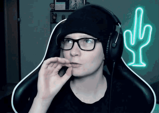 a person wearing glasses and headphones with a cactus neon sign in the background