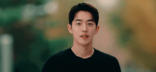 a young man in a black shirt is looking at the camera with trees in the background .