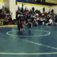 a blurry picture of a wrestling match in a gym with a crowd watching .