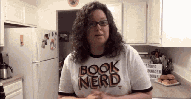 a woman wearing a book nerd t-shirt stands in a kitchen