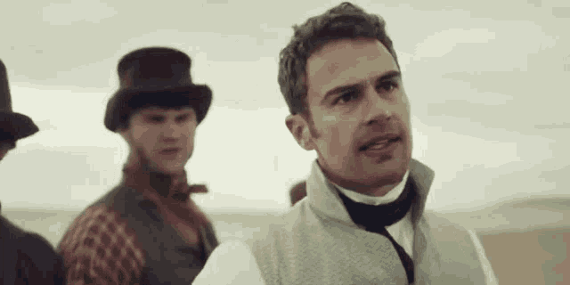 a man in a top hat stands next to another man in a vest