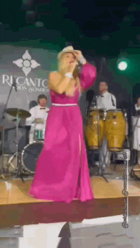 a woman in a pink dress stands on a stage in front of a sign that says ricanto