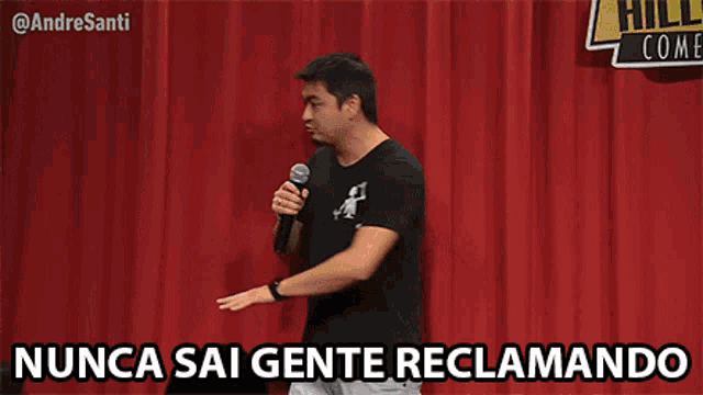 a man is holding a microphone in front of a red curtain with the words nunca sai gente reclamando below him