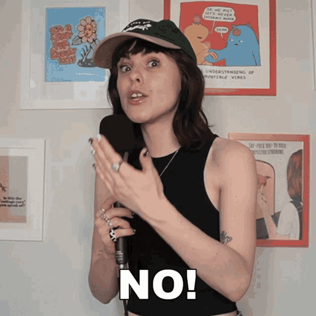 a woman wearing a hat and a black tank top holds a microphone and says no