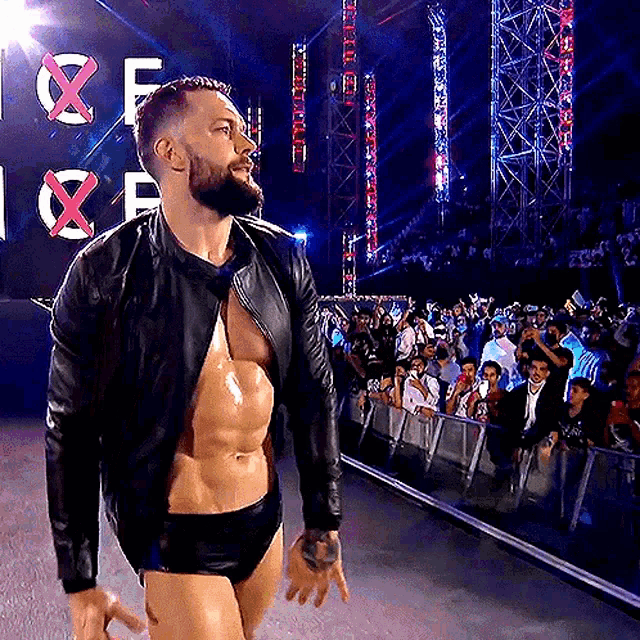 a man with a beard and a leather jacket is walking in front of a crowd at a wrestling event .