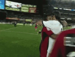 two soccer players hugging each other on a field with a scoreboard in the background