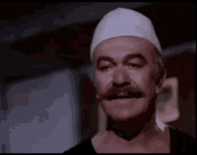 a man with a mustache is wearing a white hat and a black shirt .