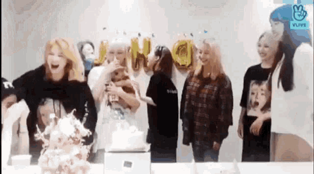 a group of women are standing around a table with a cake in front of them .
