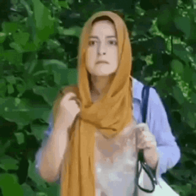 a woman wearing a yellow scarf and a blue shirt is standing in a forest .