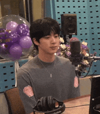 a man wearing headphones is sitting in front of a microphone with purple balloons behind him