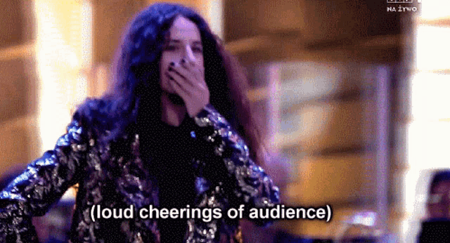 a woman in a sequined jacket is covering her mouth and saying loud cheering of audience .
