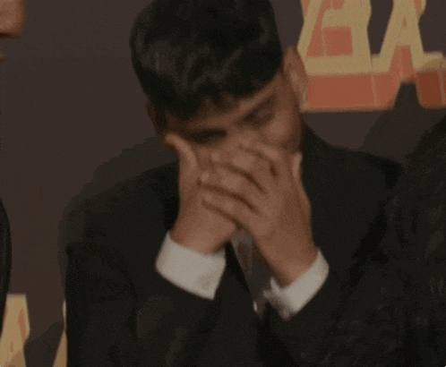 a man covering his mouth with his hands in front of a sign that says " the bay "