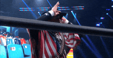 a man wearing an american flag and a hat stands in front of a row of blue seats