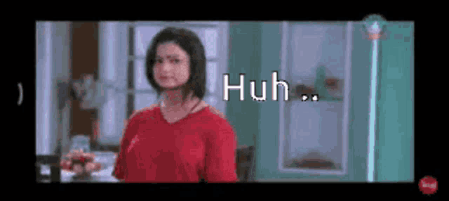 a woman in a red shirt is standing in front of a window with the words huh written on it .