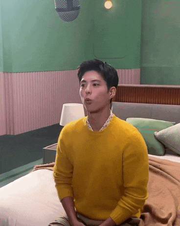 a young man wearing a yellow sweater is sitting on a bed