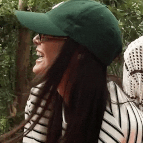 a woman wearing a green hat and sunglasses is laughing .