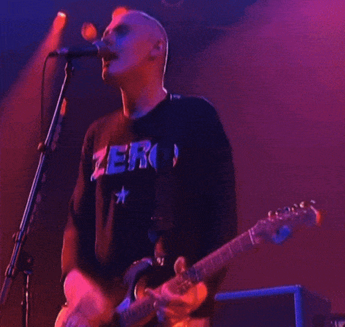 a man playing a guitar and singing into a microphone with a shirt that says zero