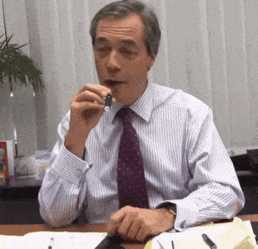 a man in a striped shirt and purple tie sits at a desk with a pen in his mouth