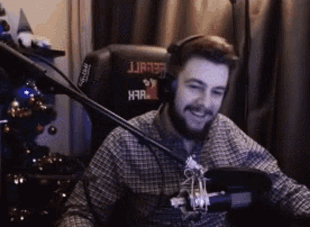 a man wearing headphones and a plaid shirt is sitting in front of a microphone and smiling .