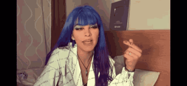 a woman with blue hair is sitting on a bed smoking a cigarette ..