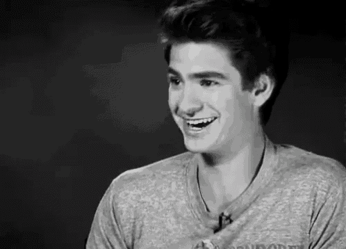 a young man is smiling in a black and white photo while wearing a grey shirt .