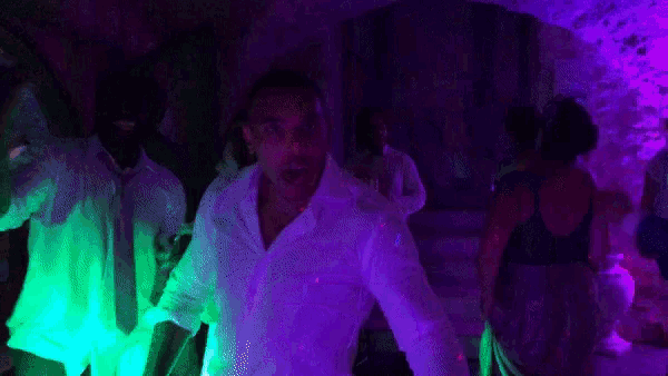 a man in a white shirt is dancing in a dark room with purple lights