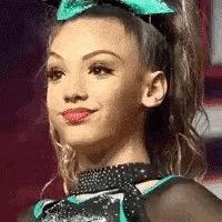 a cheerleader with a green bow in her hair is smiling and wearing a choker .