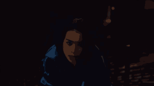 a woman in a blue jacket is standing in the dark looking at the camera