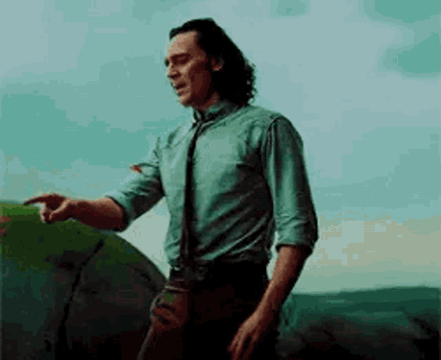 a man in a green shirt and tie is pointing at something while standing on top of a rock .