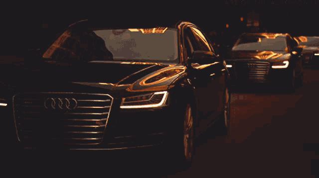 two black audi cars are parked next to each other on a dark road