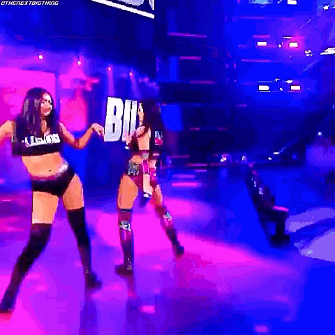 two women are dancing on a stage in a dark room with purple lights .