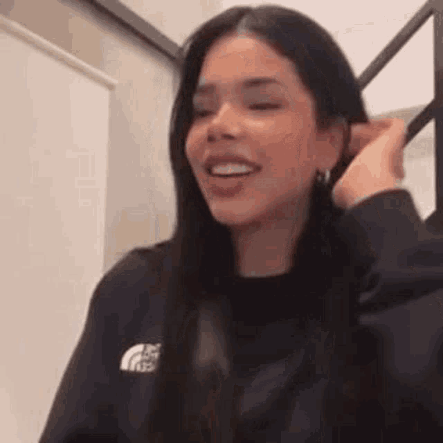 a woman is smiling and touching her hair while wearing a black sweater and earrings .