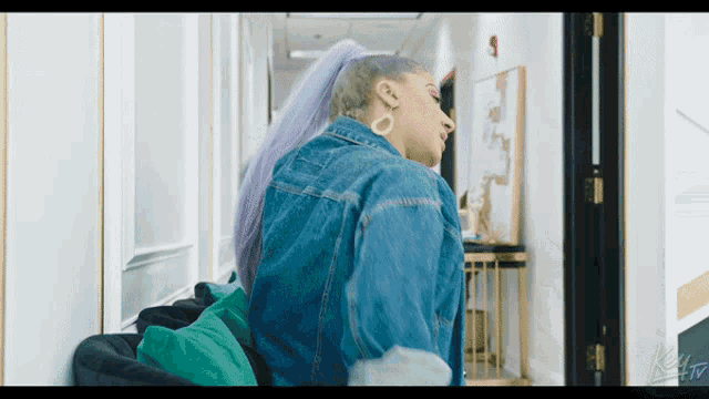 a woman with purple hair is wearing a denim jacket and earrings
