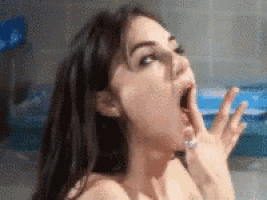 a woman is yawning with her mouth open and her hands on her face .