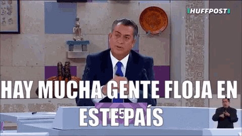 a man in a suit and tie is speaking into a microphone with the words hay mucha gente floja en este pais below him