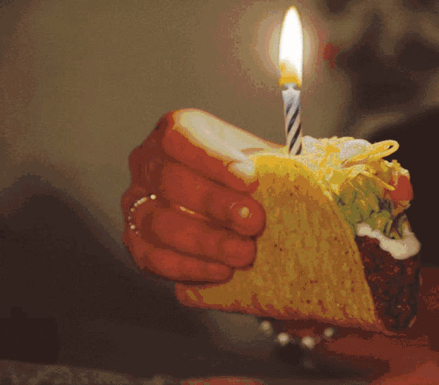 a person holding a taco with a lit candle on top