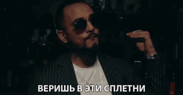 a man with a beard and sunglasses is holding a glass of wine in his hand .