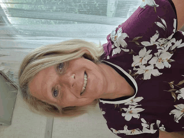 a woman wearing a purple shirt with white flowers on it smiles for the camera