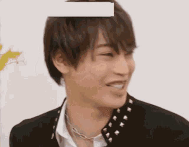 a young man wearing a black jacket with studs on the collar and a necklace is smiling .