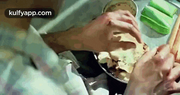 a close up of a person 's hands holding a bowl of food on a table .
