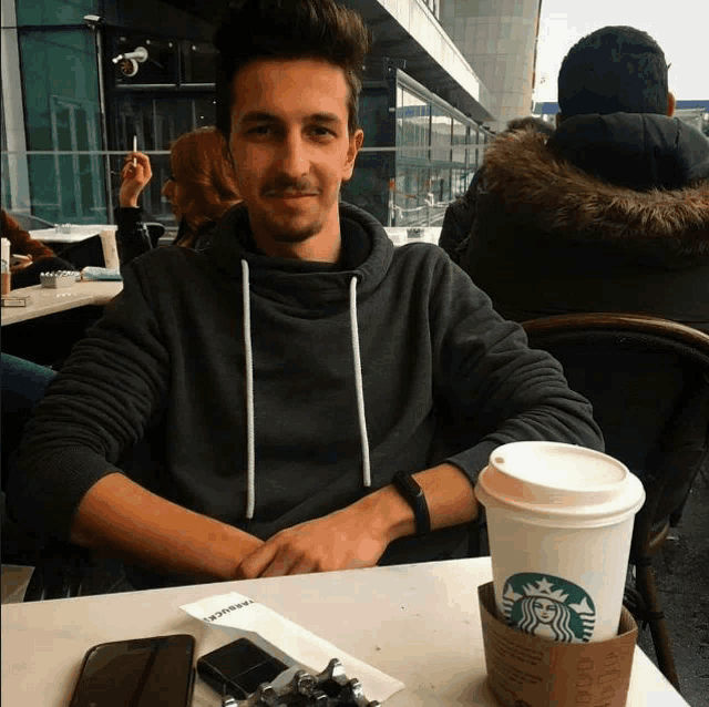 a man sitting at a table with a starbucks cup