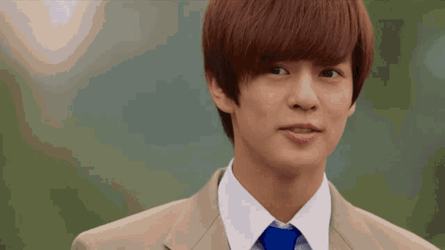 a young man in a tan suit and blue tie looks at the camera